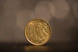 A shiny gold coin from the 1800s displayed against a soft, blurred background.