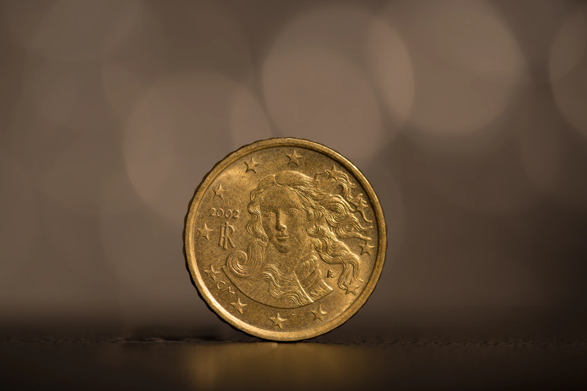High-resolution photo of a golden commemorative coin shining under warm light with subtle watermark textures in the background.