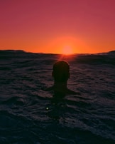 Sunset view of a freediver surfacing, the sky painted with warm orange and pink hues.
