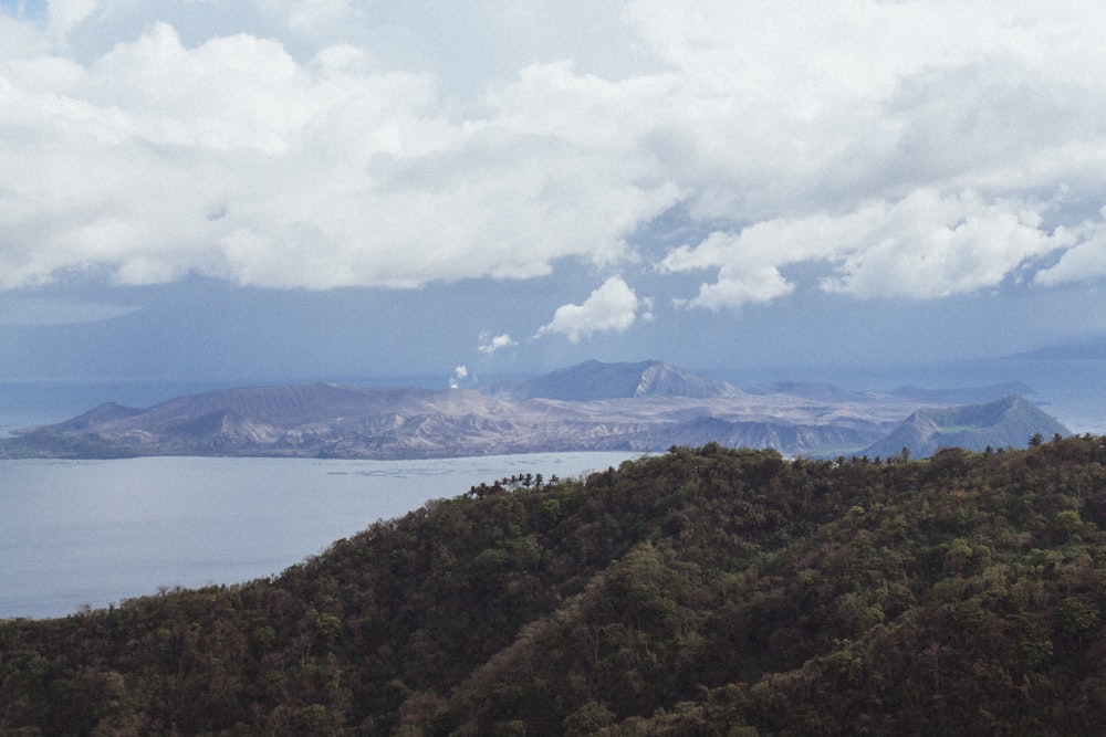 montaña verde cerca del cuerpo de agua bajo nubes blancas y cielo azul durante el día