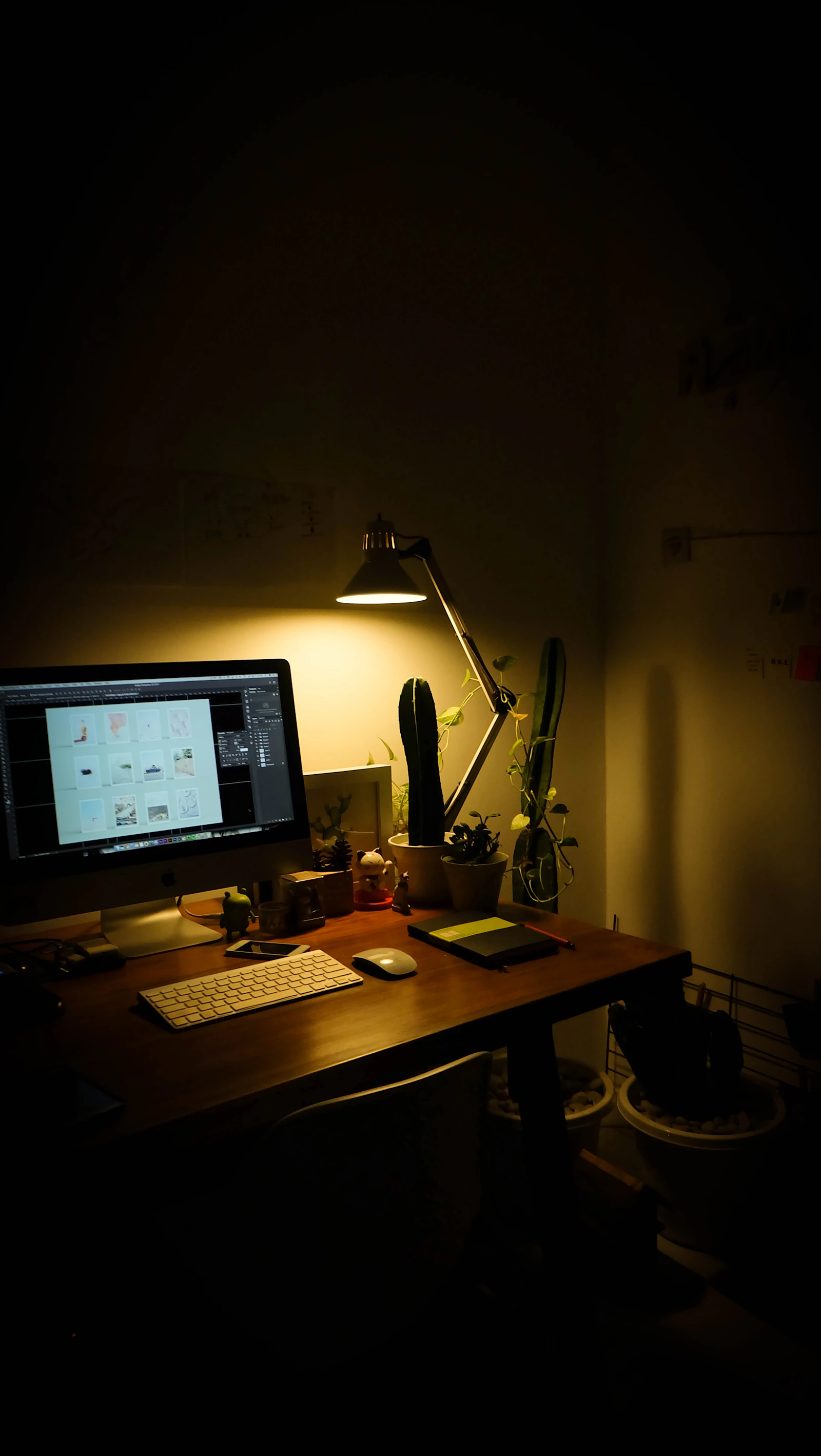 Warm dark home office with a monitor, desk lamp, and plants