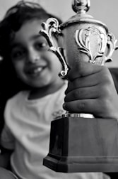 A smiling child celebrating a chess victory with a trophy.