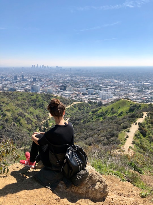 woman in black shirt sitting on rock looking at the sea during daytime in Runyon Canyon Park United States