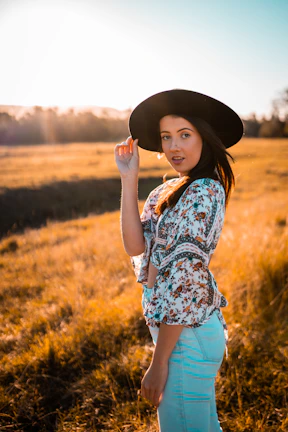Model wearing a blue chambray shirt and a wide-brimmed hat, standing in a sunlit ranch field
