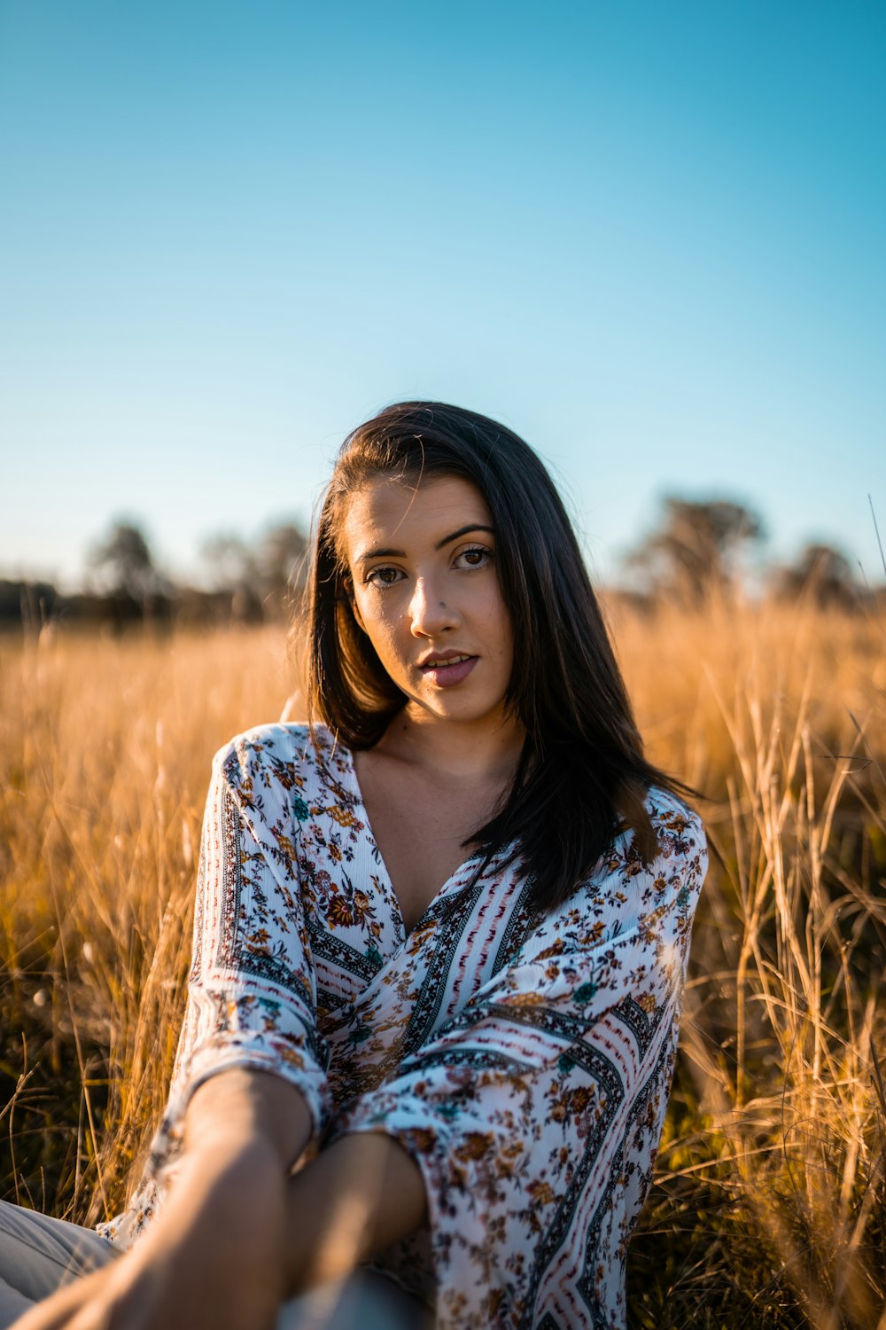 woman in blue and white floral long sleeve shirt standing on brown grass field during daytime