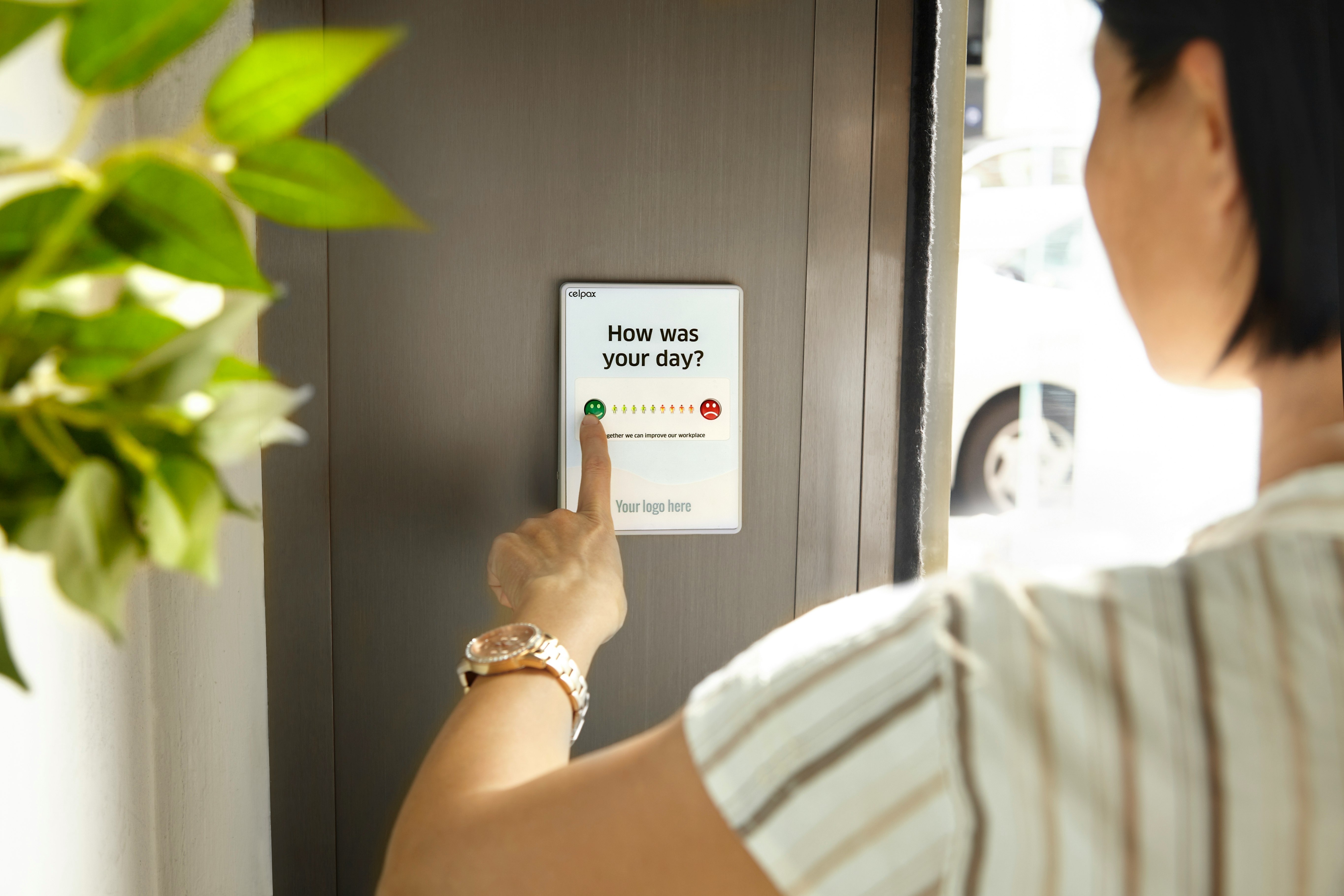 Female employee pressing a green button to give feedback on a device at the company exit door