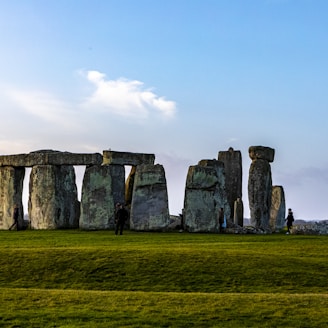 gray rock formation on green grass field under white clouds during daytime