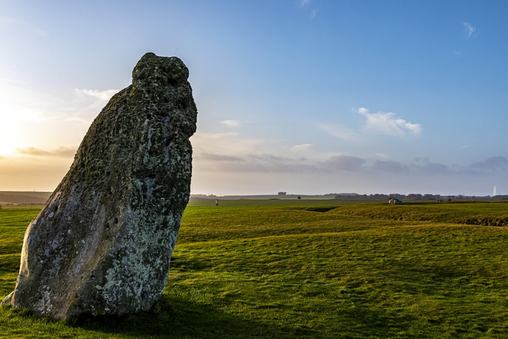 gray rock formation on green grass field under white clouds and blue sky during daytime