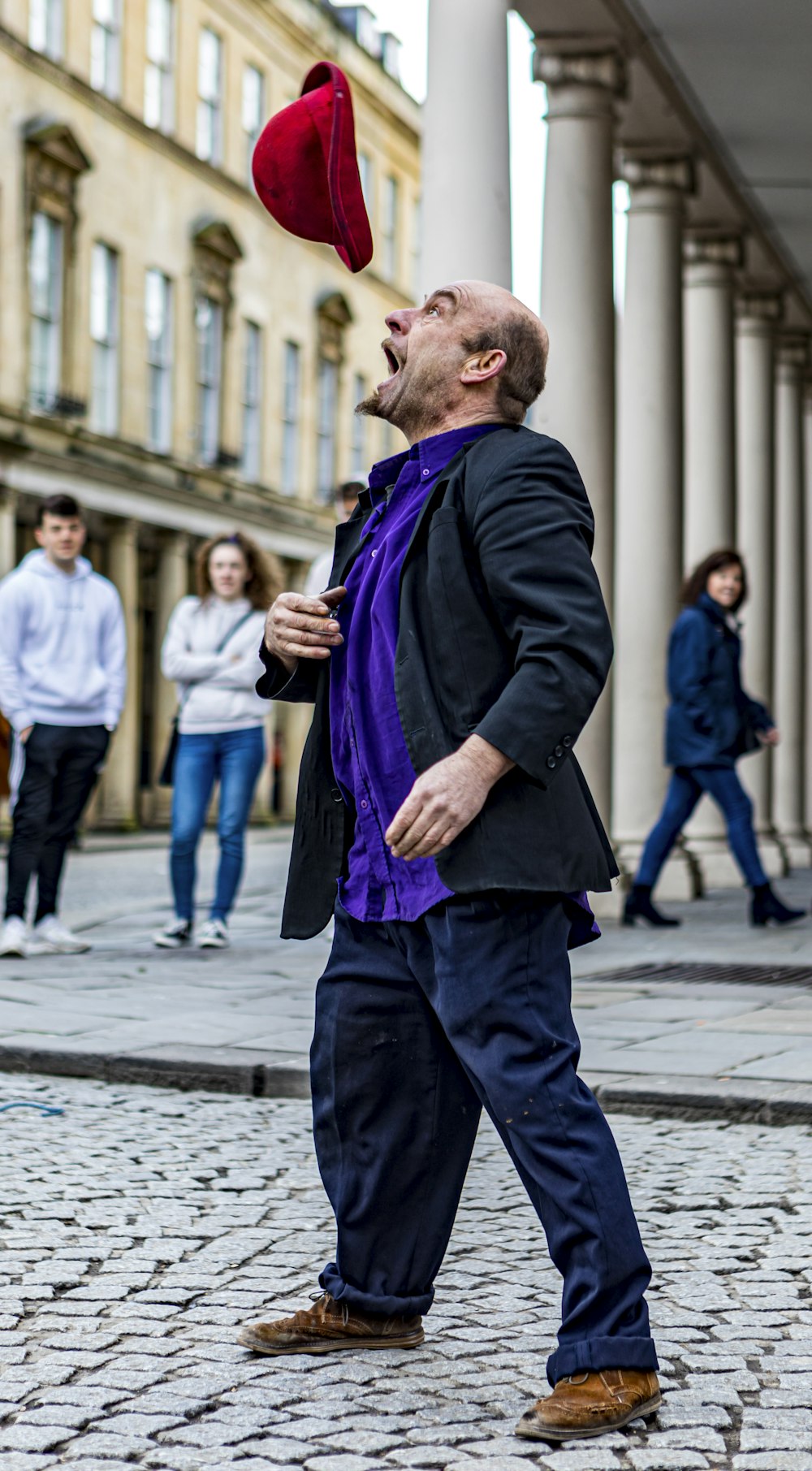 man in black suit jacket and purple scarf standing on sidewalk during daytime