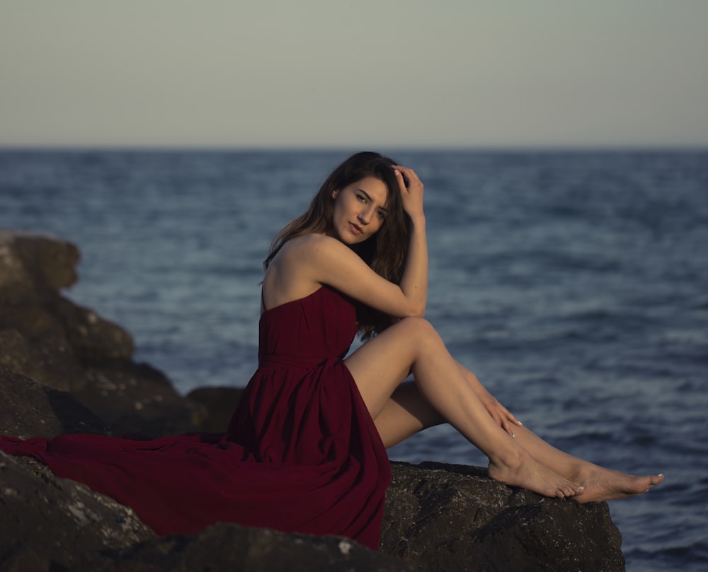woman in red dress sitting on rock near sea during daytime