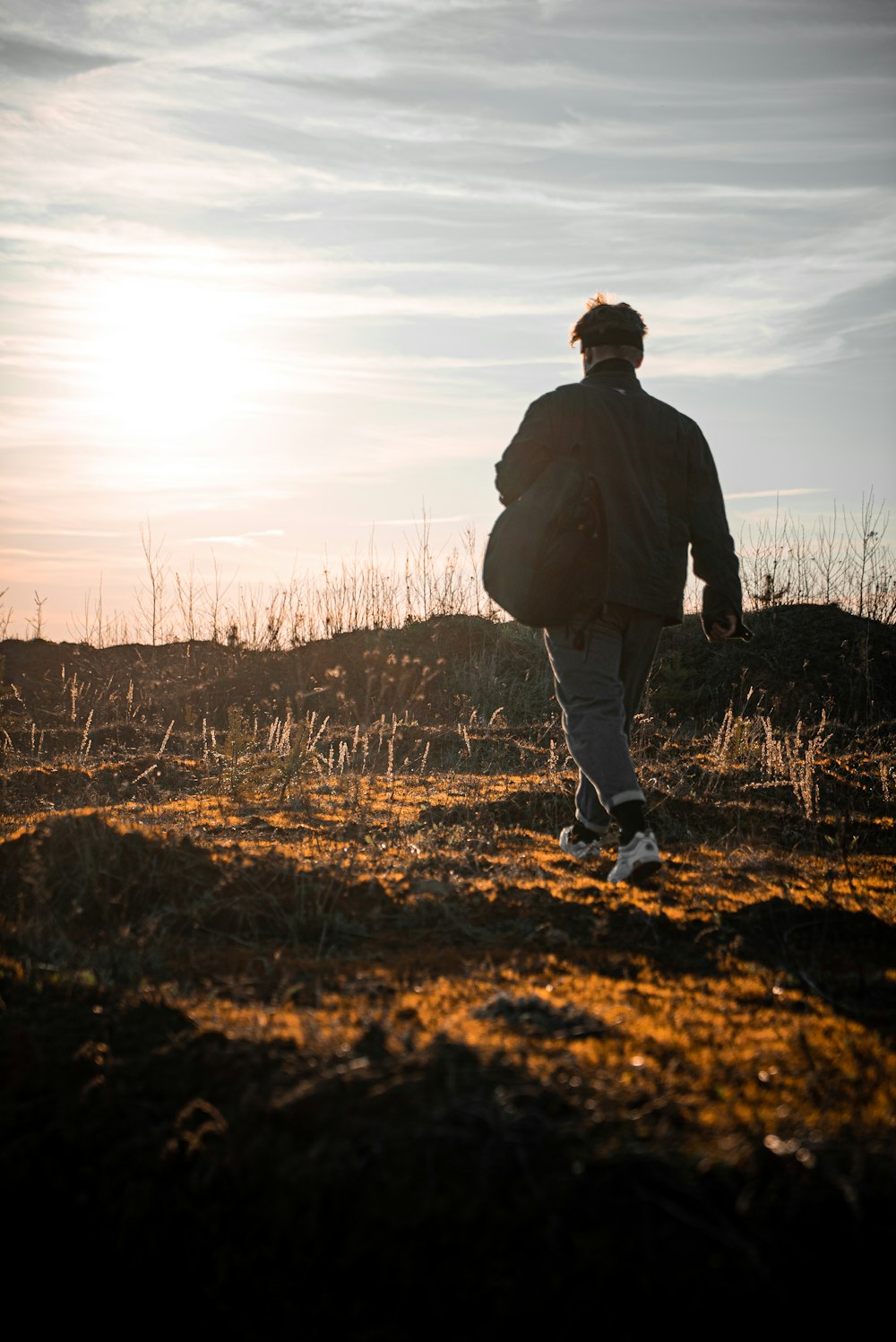 Hombre con chaqueta negra caminando en el campo de hierba marrón durante el día