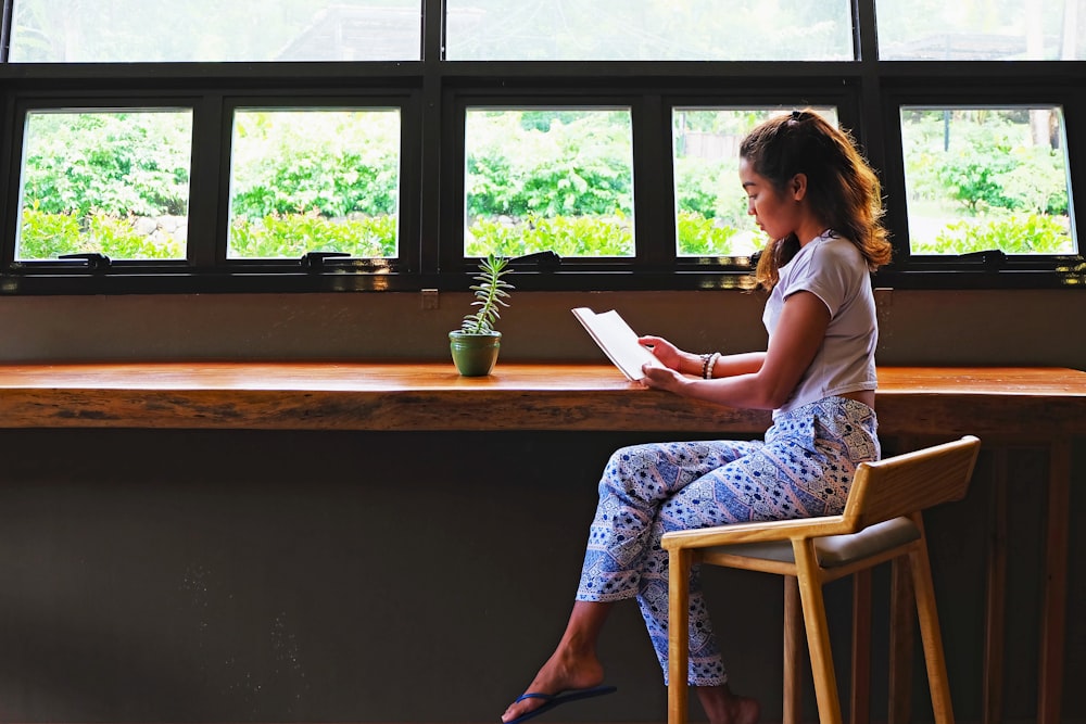 woman in white shirt sitting on chair reading book