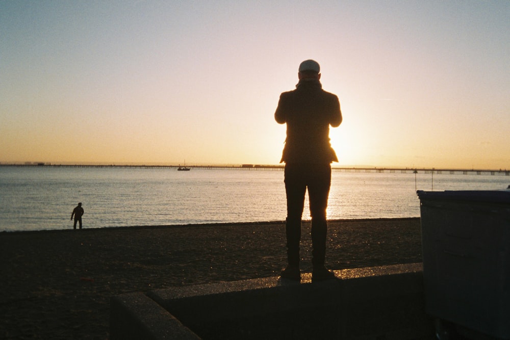 Silueta del hombre de pie en la playa durante la puesta del sol