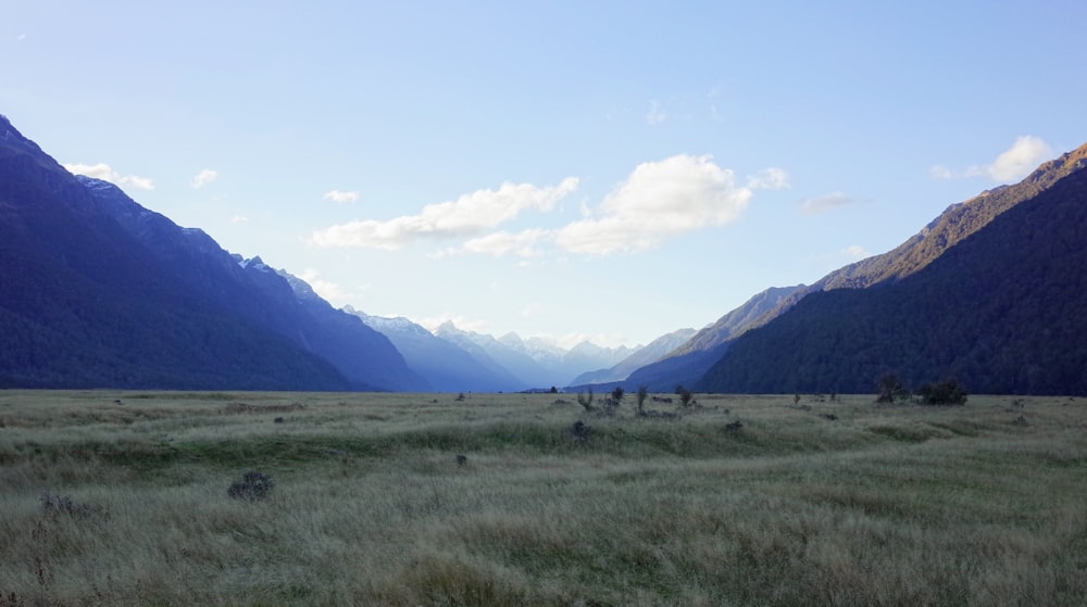 green grass field near mountain under white clouds during daytime