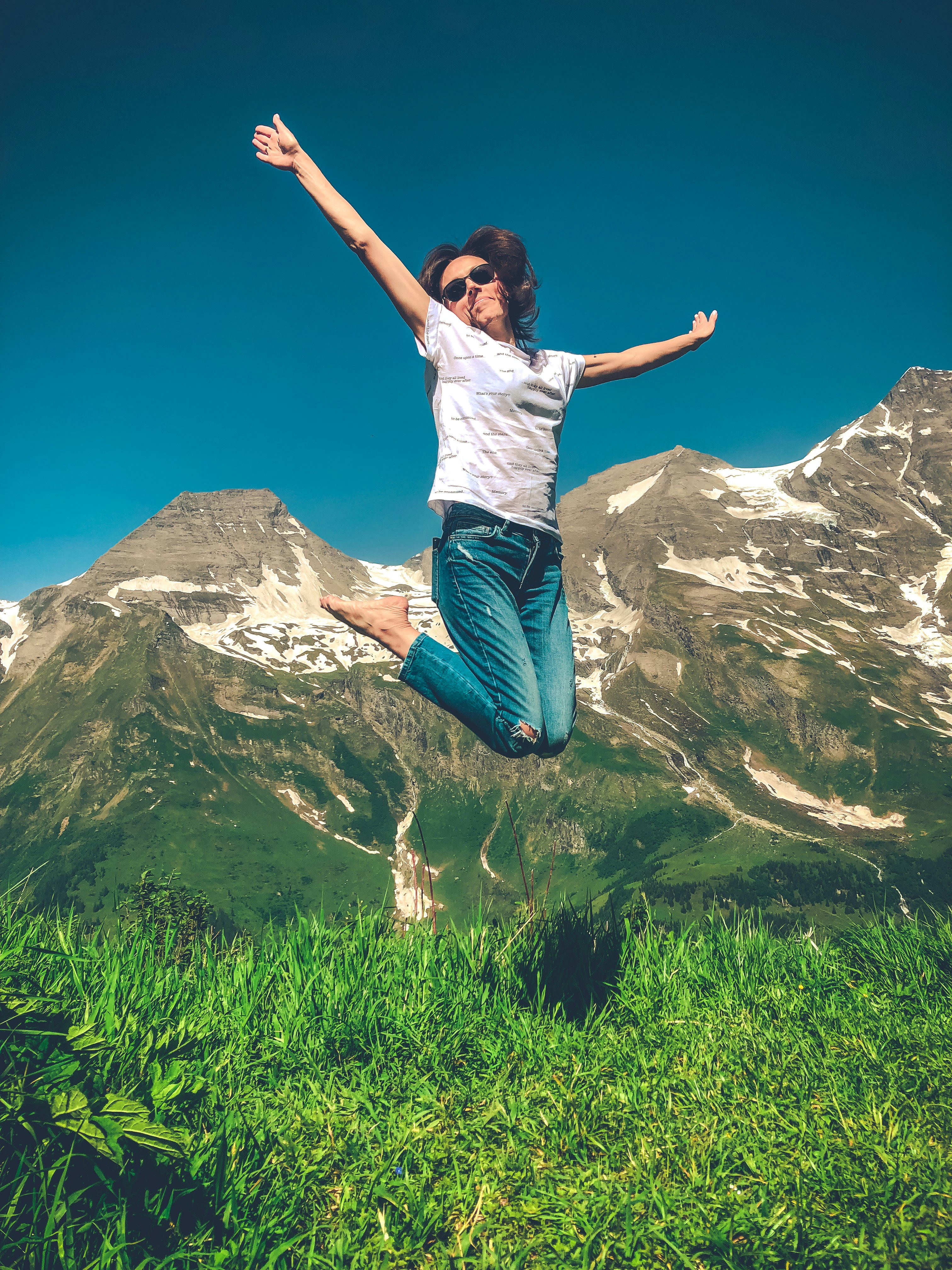 woman in white shirt and blue denim jeans jumping on green grass field during daytime