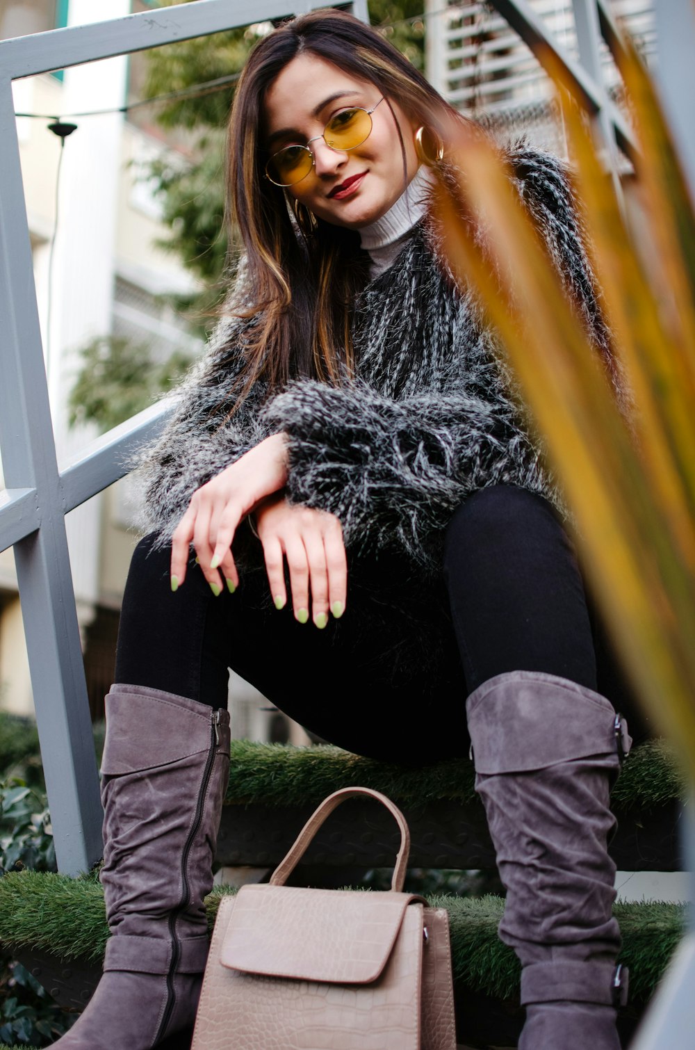 woman in gray fur coat and black pants sitting on yellow metal bar during daytime