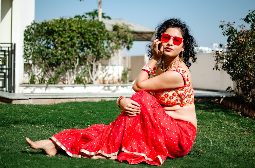 woman in red and white floral sleeveless dress sitting on green grass field during daytime