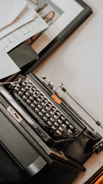 A monochrome photo of a vintage typewriter with scattered pages, bathed in soft gray light.