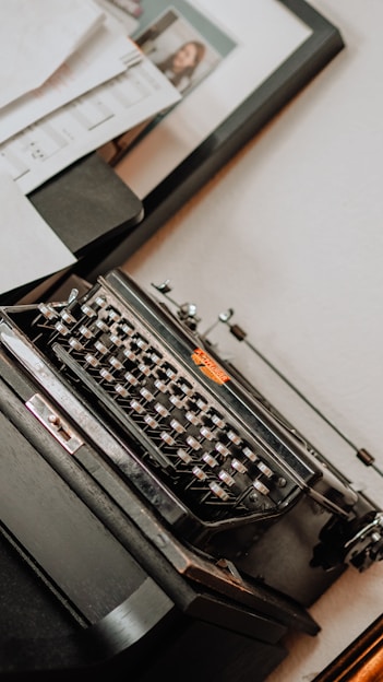 A moody, elegant black and tan photo of Maris James at a vintage typewriter, surrounded by stacks of manuscripts.