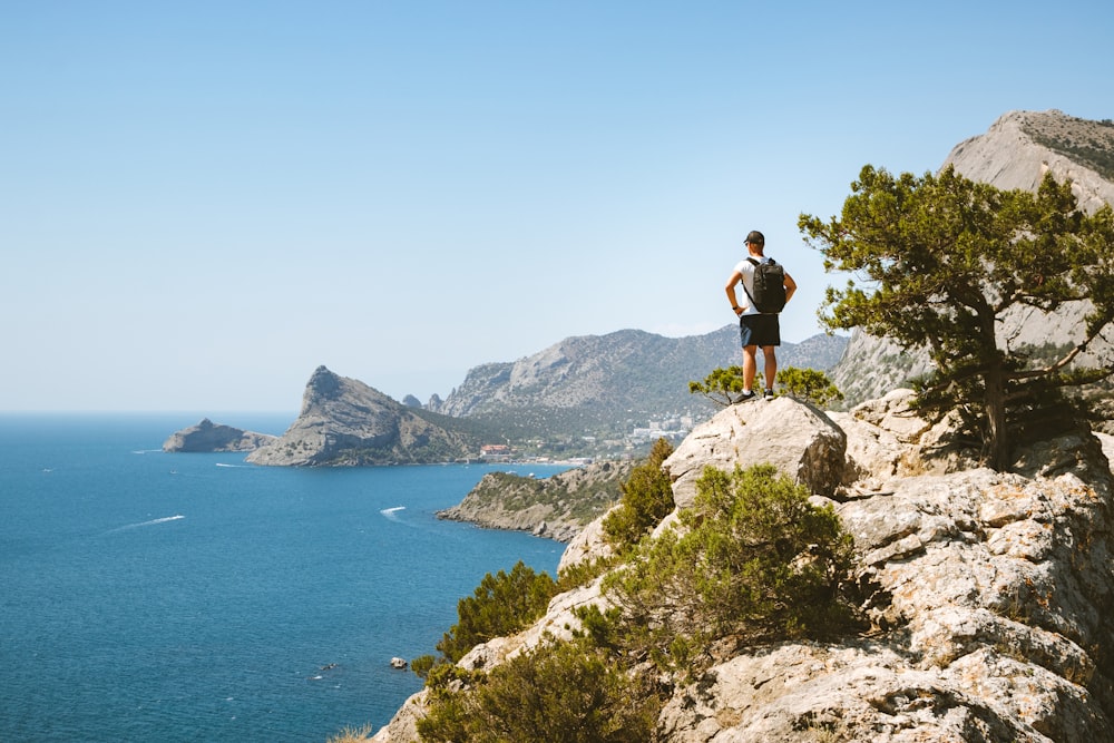 man in black shirt standing on rock formation near body of water during daytime