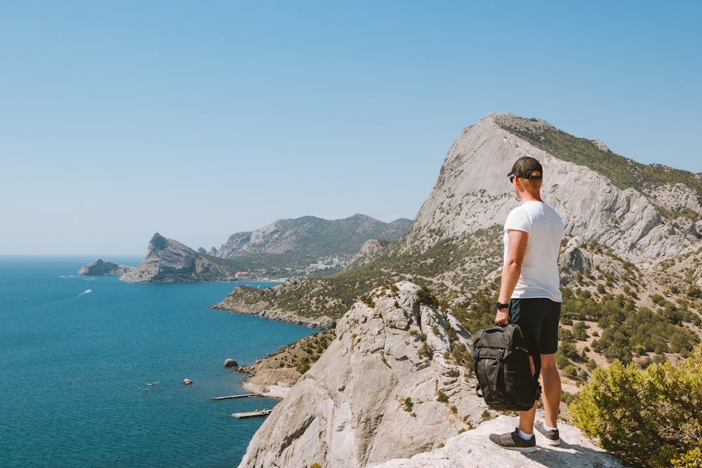 man in white t-shirt standing on rocky mountain during daytime