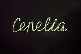 Neon green cursive letters form the word 'Cepelia' against a dark background.