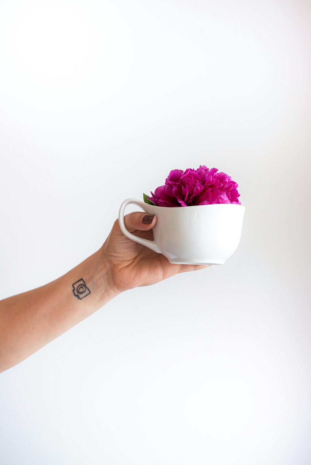 person holding white ceramic mug with pink flowers