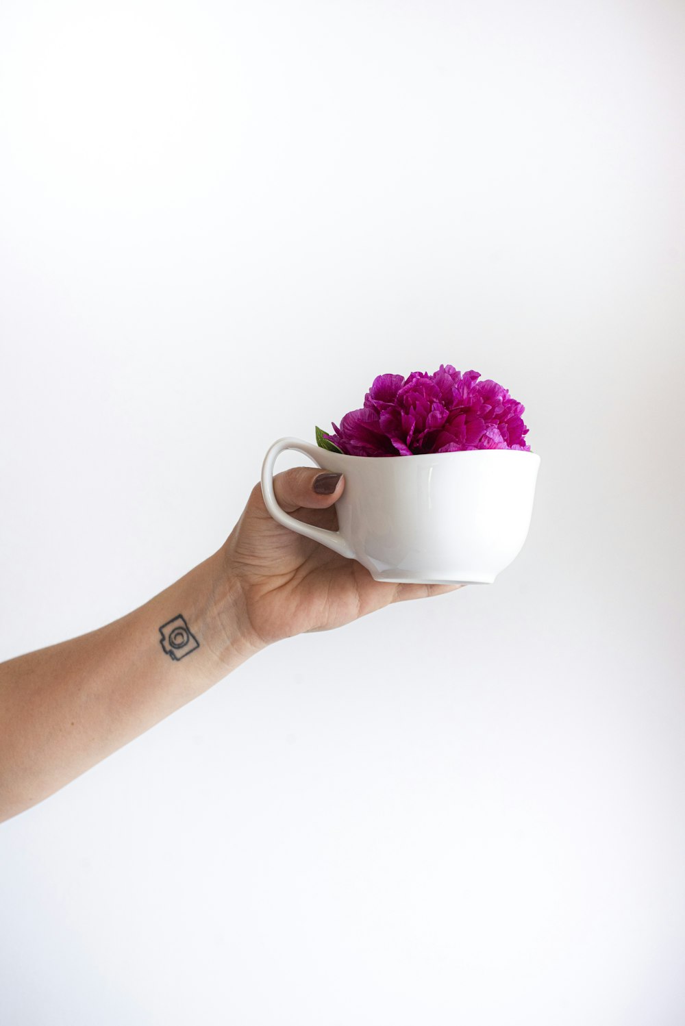 personne tenant une tasse en céramique blanche avec des fleurs roses