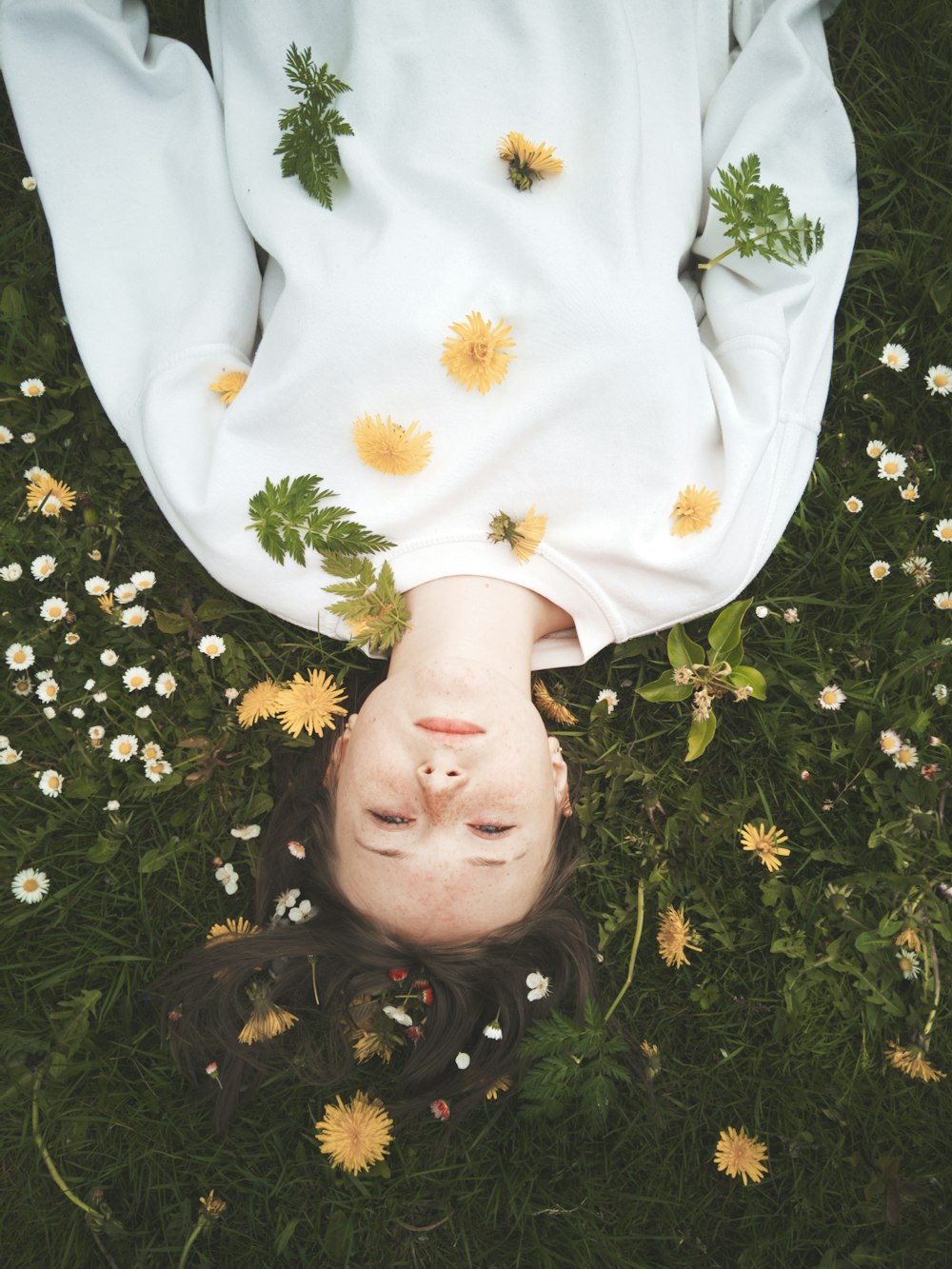 girl in white and yellow floral long sleeve shirt lying on green grass field