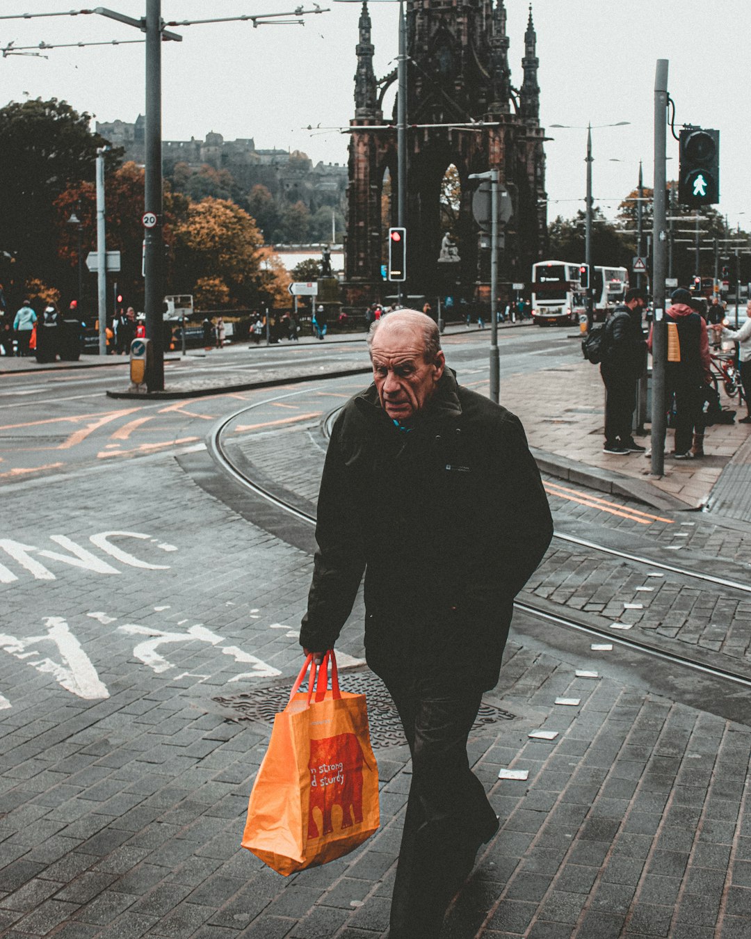 man in black coat holding orange plastic bag standing on sidewalk during daytime