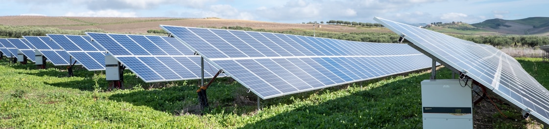 blue solar panels on green grass field under white clouds and blue sky during daytime