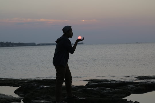 man in black jacket and brown pants standing on brown rock near body of water during in Lamongan Indonesia