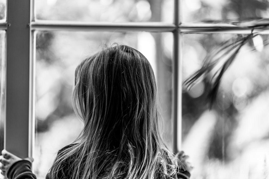 grayscale photo of woman looking at the window