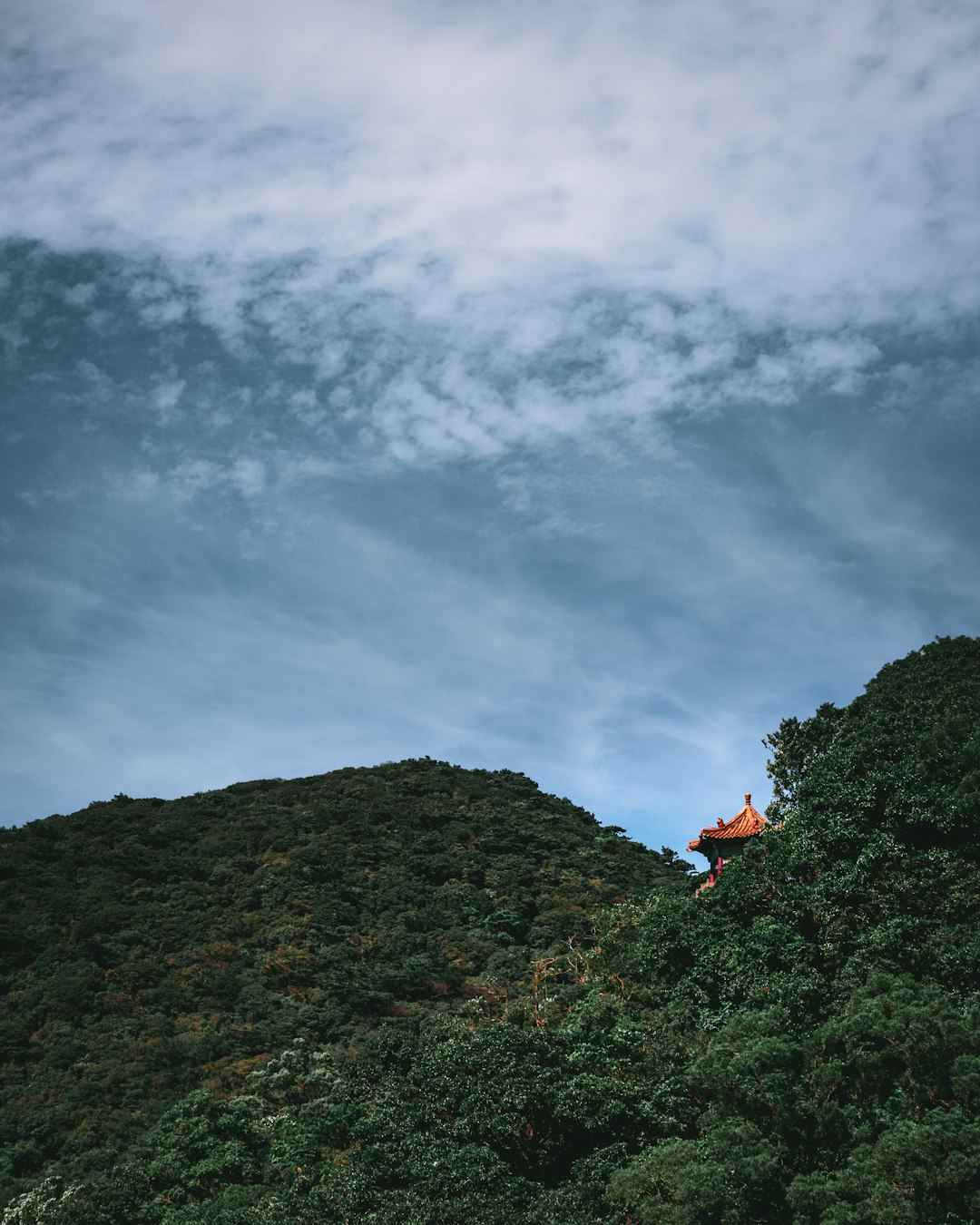 person in red jacket sitting on rock mountain under cloudy sky during daytime