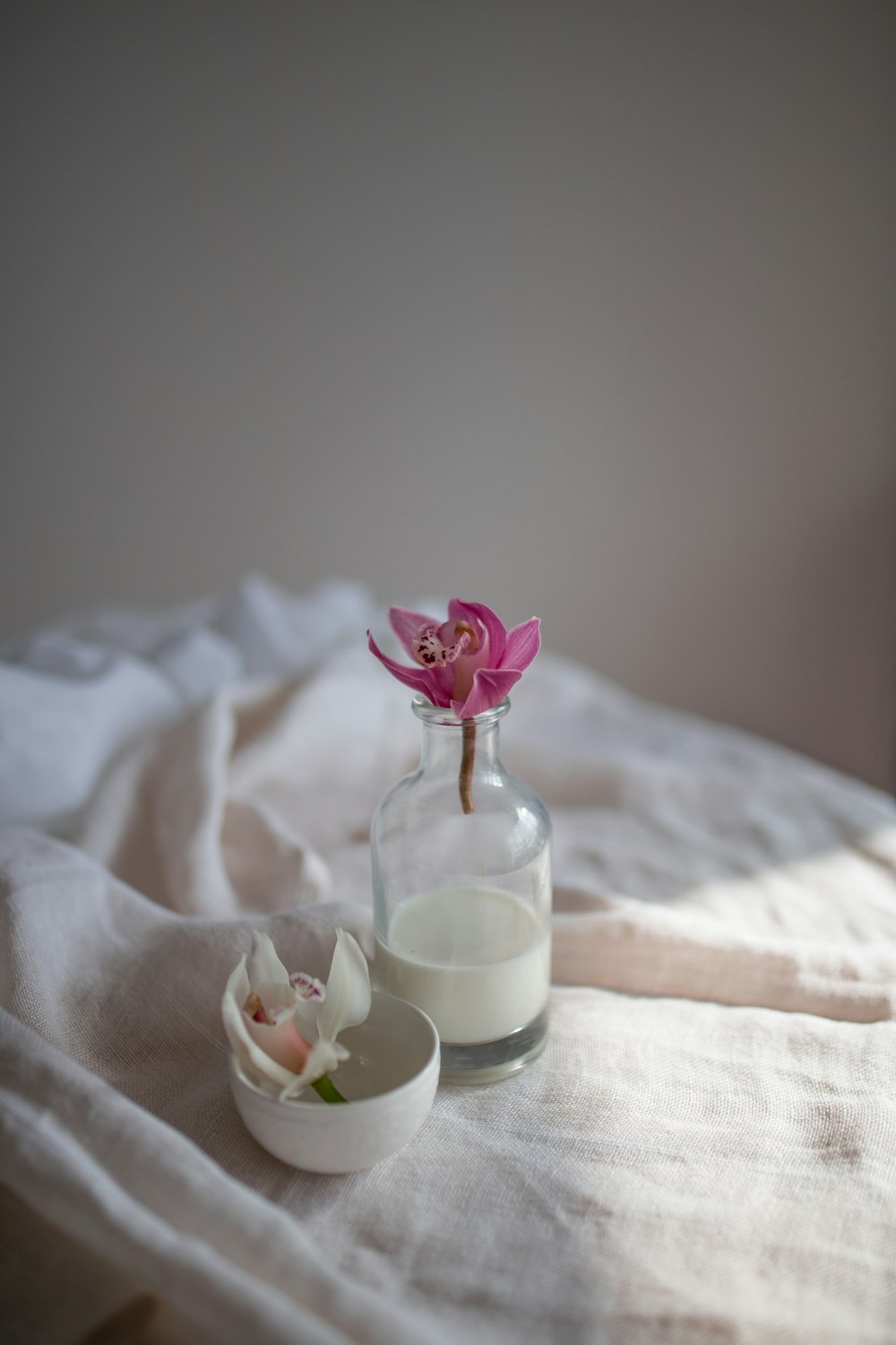 pink rose in clear glass jar on white textile