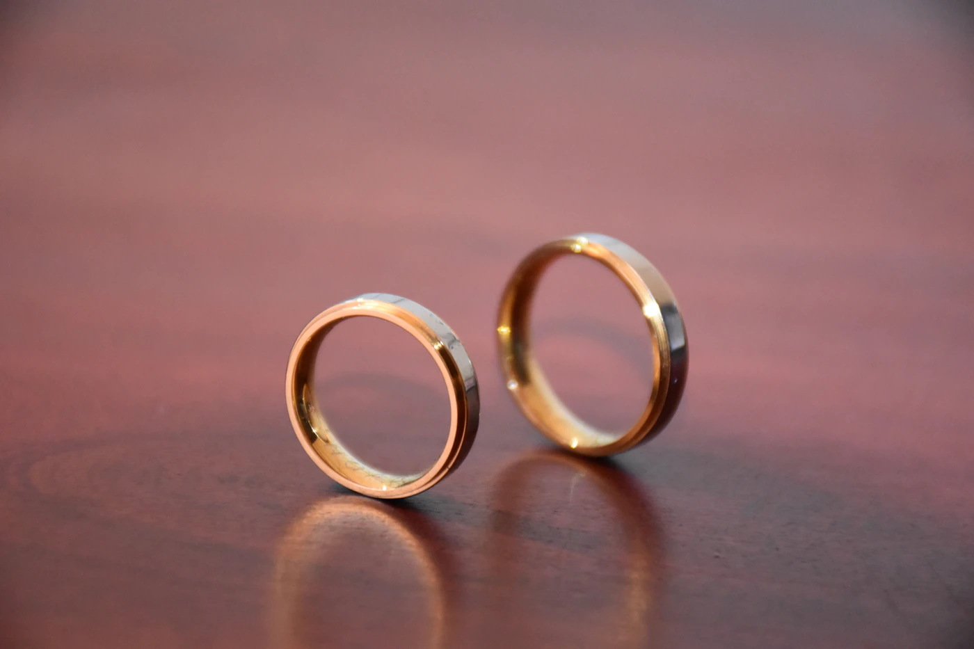 Two gold wedding bands standing upright on a polished wooden surface