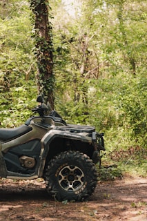 A rugged ATV parked on a forest trail with autumn leaves scattered around.