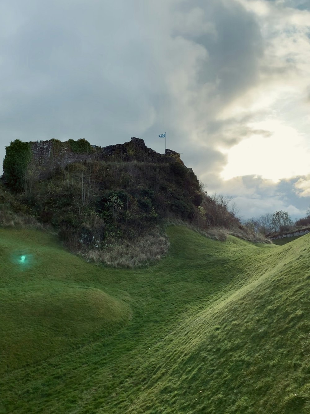 Grünes Grasfeld in der Nähe von grauer Felsformation unter grauem Himmel tagsüber