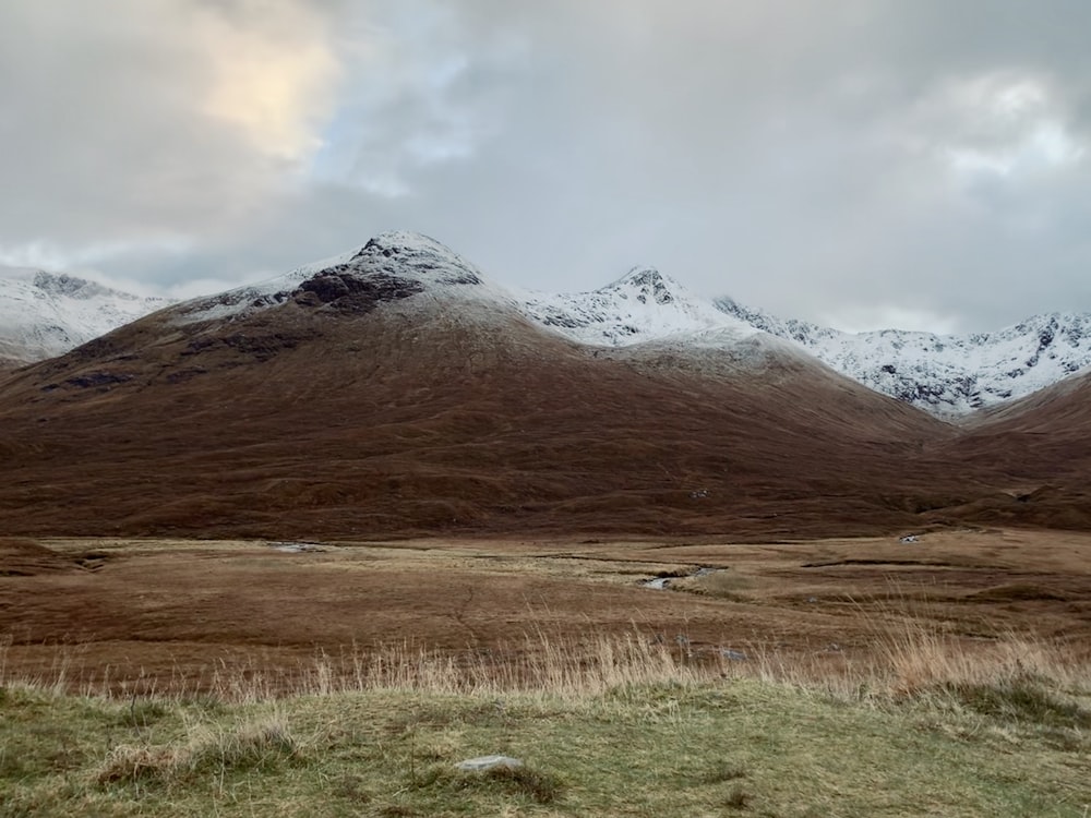 brown grass field near snow covered mountain during daytime