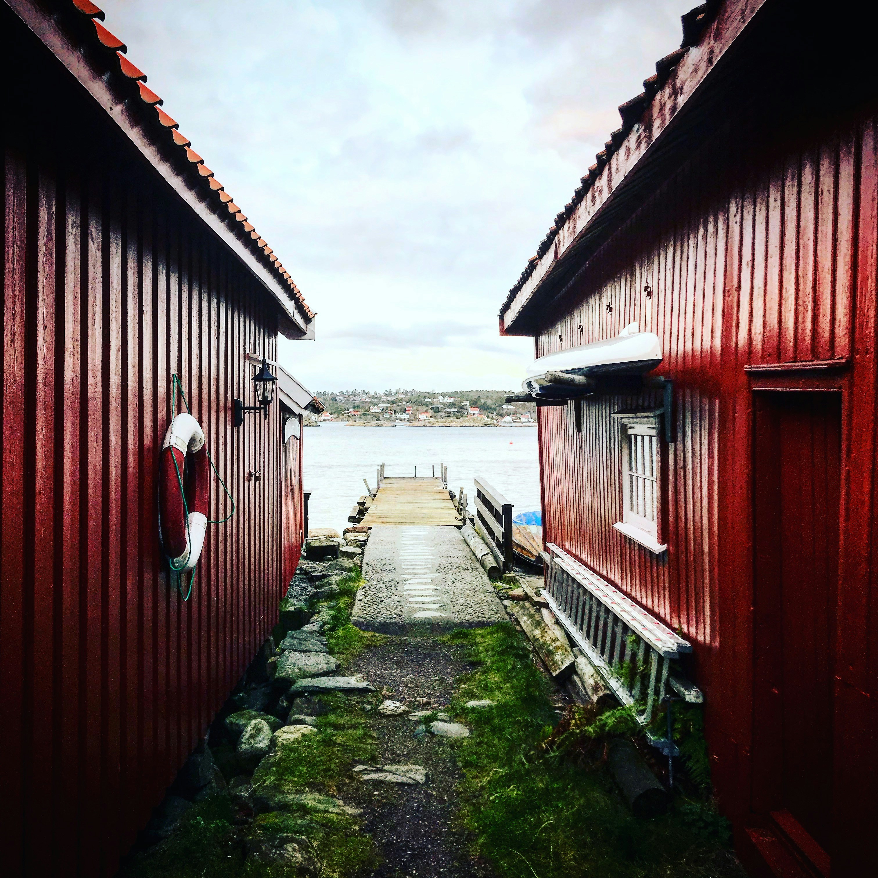 Maison en bois rouge près du plan d’eau sous des nuages blancs pendant la journée