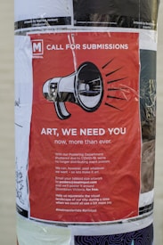 A poster on a wall featuring a red background with a megaphone graphic. It includes a call for submissions for art due to COVID-19 disrupting regular postering activities. The poster invites artists to email their artwork for free distribution in downtown Victoria, encouraging art to rejuvenate the visual landscape during these challenging times.