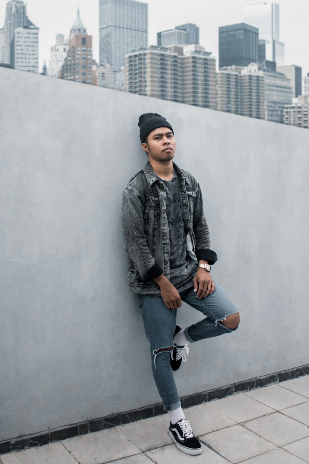 man in black leather jacket and blue denim jeans sitting on concrete wall