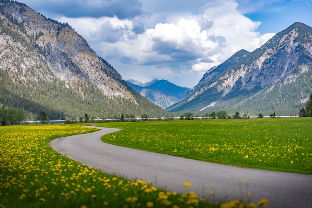 green grass field near mountain under white clouds during daytime