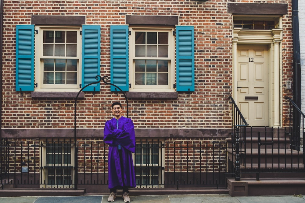 woman in purple coat standing in front of brown brick building