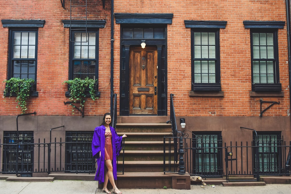 woman in purple long sleeve shirt and black pants standing near brown wooden door