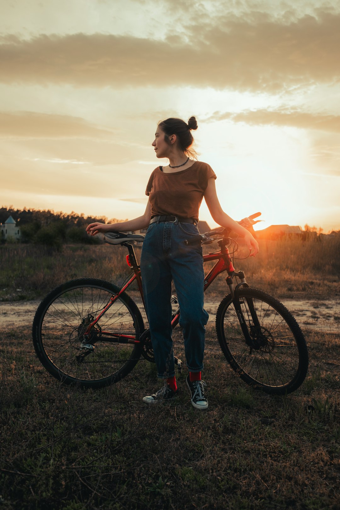 woman in brown tank top and blue denim jeans standing beside black bicycle during sunset