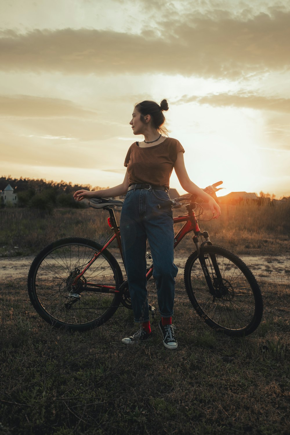 woman in brown tank top and blue denim jeans standing beside black bicycle during sunset
