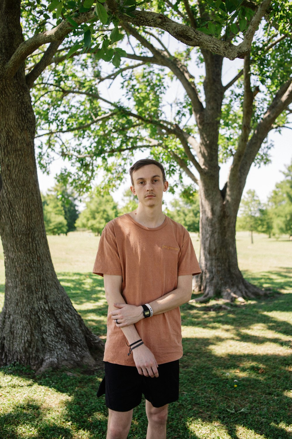 man in brown crew neck t-shirt standing beside tree during daytime