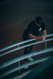 man in black t-shirt and black cap leaning on white metal railings