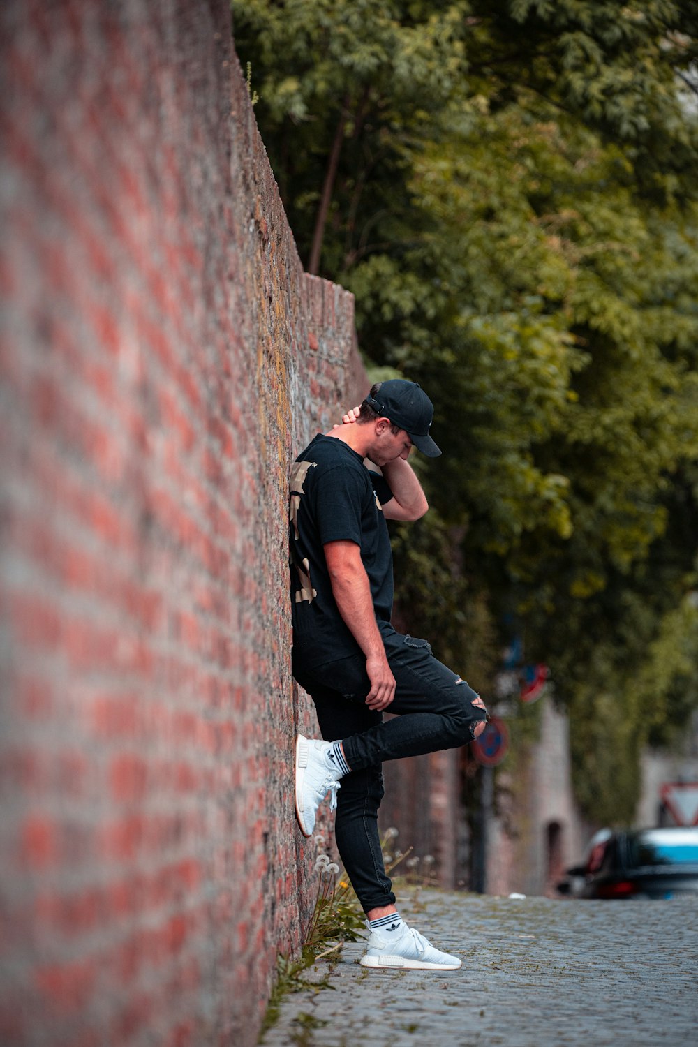 man in black t-shirt and black pants leaning on red brick wall during daytime